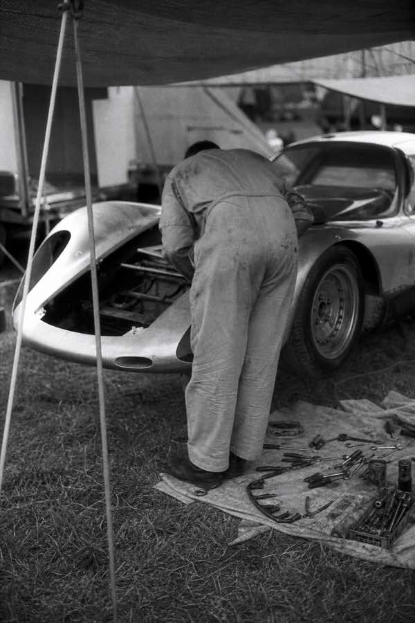 A mechanic working on the engine of a racing car in a paddock